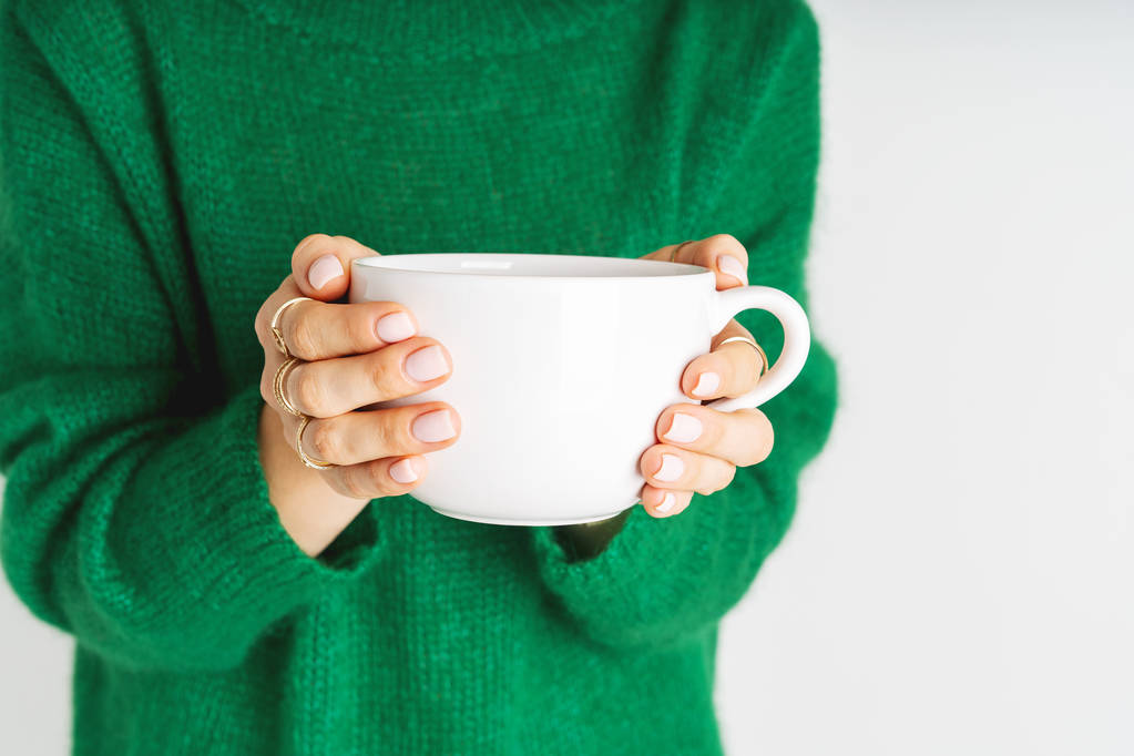 手に大きな白いマグカップを保持暖かいウールグリーンのセーターの女性 - 写真・画像