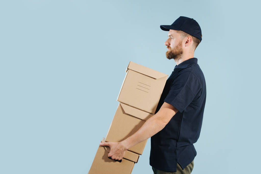 Delivery man in uniform is holding stack of cardboard boxes - Photo, Image