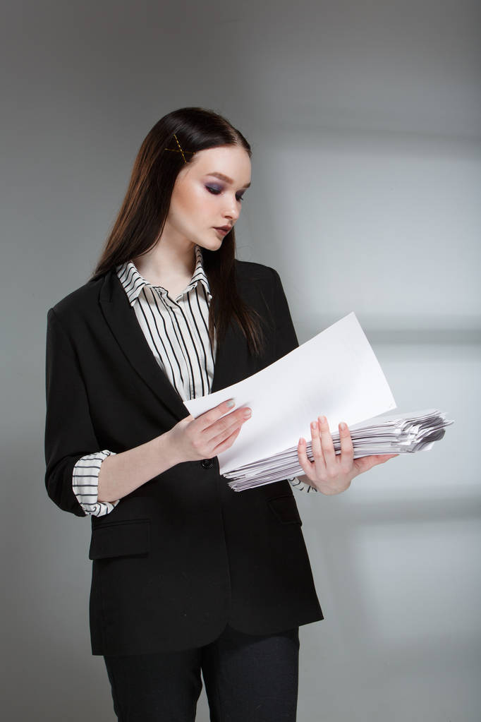 junge schöne weibliche Mode-Modell in einem Business-stilvollen Anzug auf einem Wiederholungshintergrund. hält einen Stapel Papiere und einen Stift. - Foto, Bild