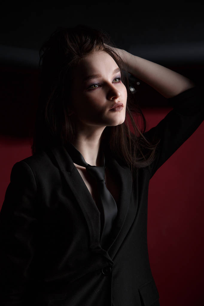 Joven modelo de moda femenina hermosa en un traje elegante de negocios sobre un fondo rojo y negro
. - Foto, imagen