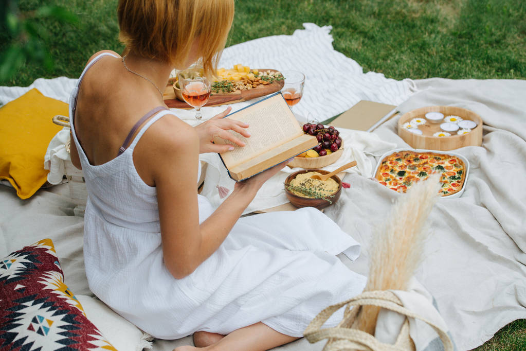Mujer joven está leyendo un libro, sentada sobre sus piernas, en un paño blanco en el picnic
 - Foto, imagen