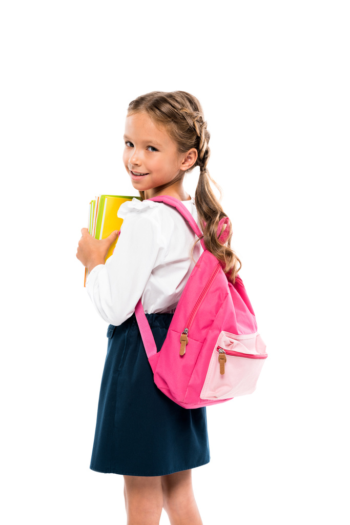 幸せな子供が本を持ち、白に隔離されたピンクのバックパックで立っている  - 写真・画像