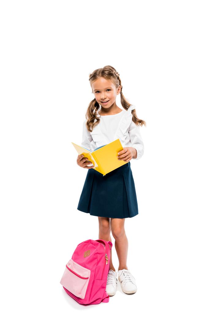 libro de lectura infantil feliz y de pie cerca de la mochila rosa aislado en blanco
  - Foto, Imagen