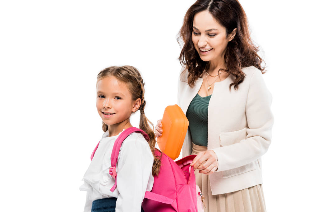 mãe atraente colocando lancheira na mochila da filha bonito isolado no branco
 - Foto, Imagem