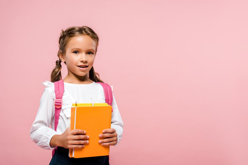 šťastný chlapec držící knihy, zatímco stojí s batohu na růžovém  - Fotografie, Obrázek