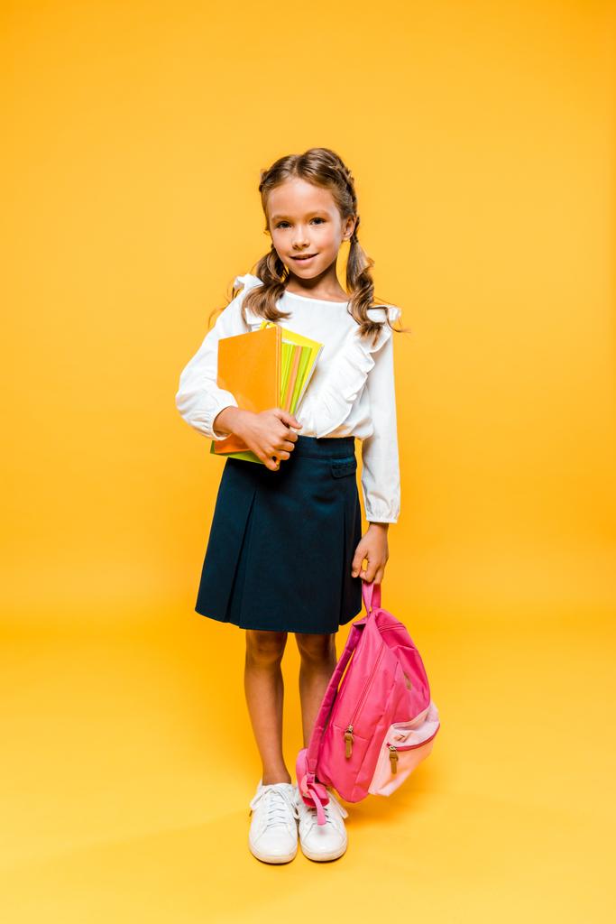 cute and happy kid holding books and backpack on orange  - Photo, Image