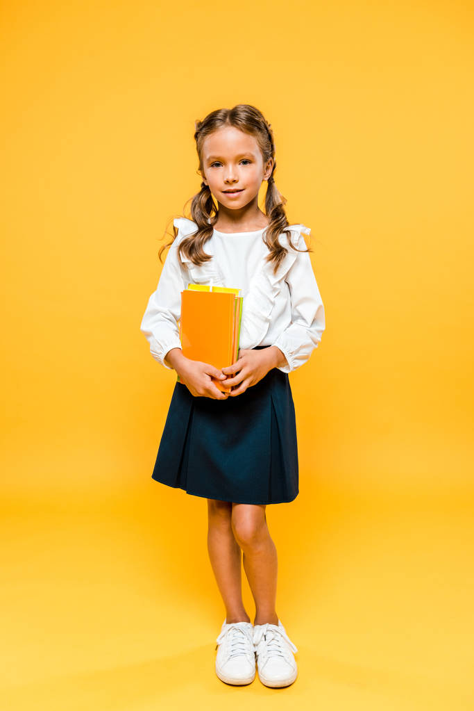 sonriente y lindo niño sosteniendo libros y de pie en naranja
  - Foto, Imagen
