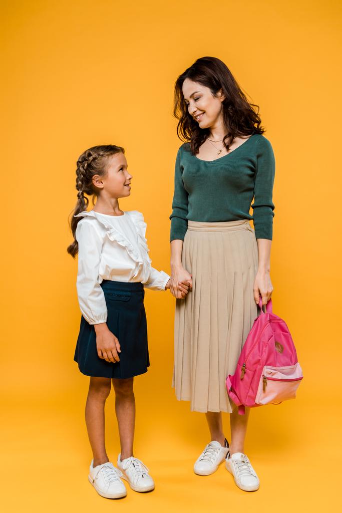 atrakcyjna matka trzyma ręce z cute uczennica na pomarańczowo  - Zdjęcie, obraz