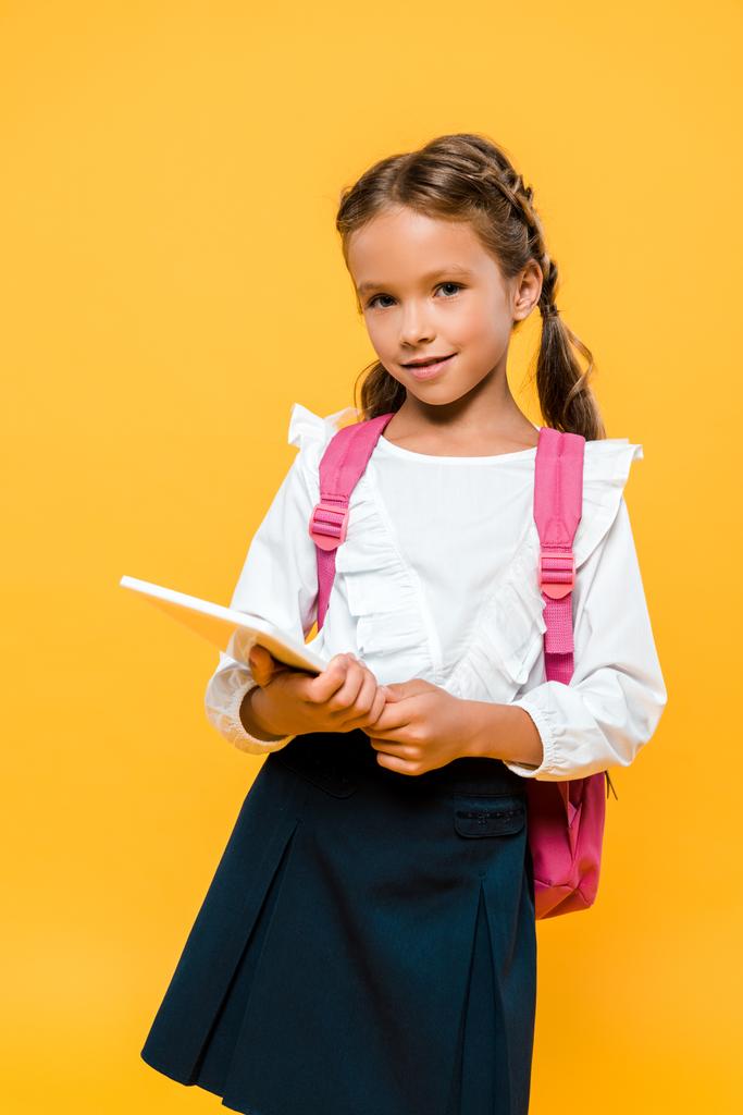 Gelukkig school kind met roze rugzak Holding boek geïsoleerd op oranje  - Foto, afbeelding