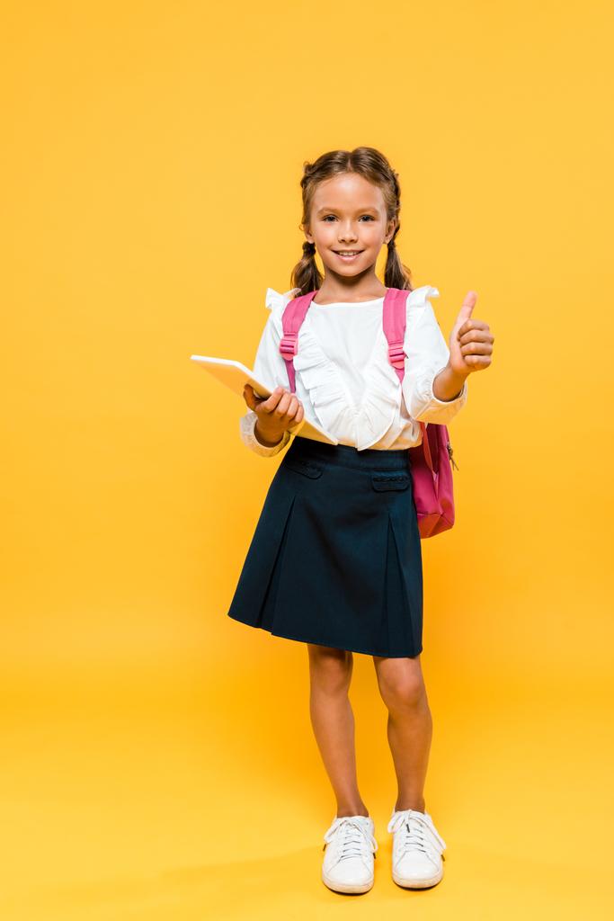 glückliches Schulkind hält Bücher in der Hand und zeigt Daumen hoch auf orange  - Foto, Bild