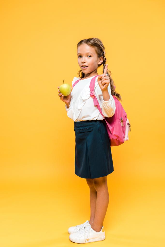 adorable colegial sosteniendo manzana y señalando con el dedo en naranja
  - Foto, imagen