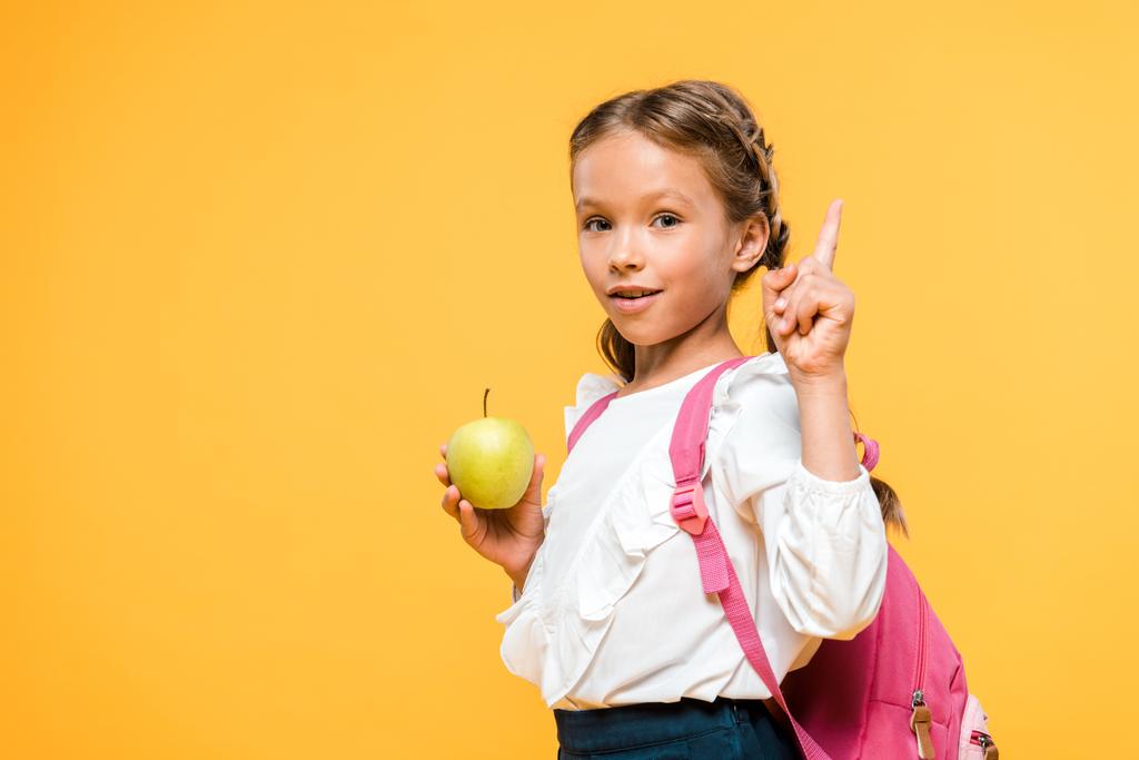adorable schoolkid holding apple and pointing with finger isolated on orange  - Photo, Image
