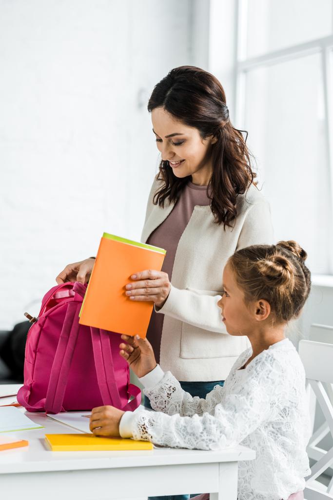 glückliche Mutter legt Buch in Rucksack der Schülerin zu Hause  - Foto, Bild