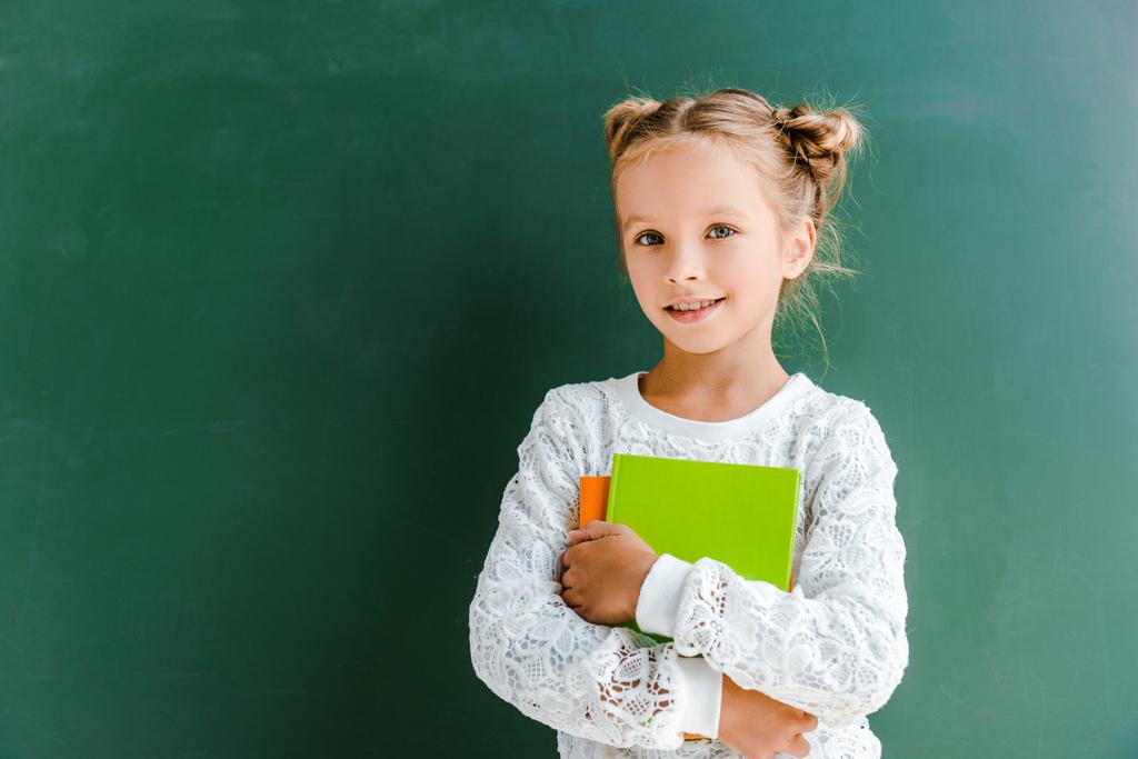 χαμογελαστή μαθήτρια χαμογελώντας ενώ στέκεται με τα βιβλία για το πράσινο  - Φωτογραφία, εικόνα