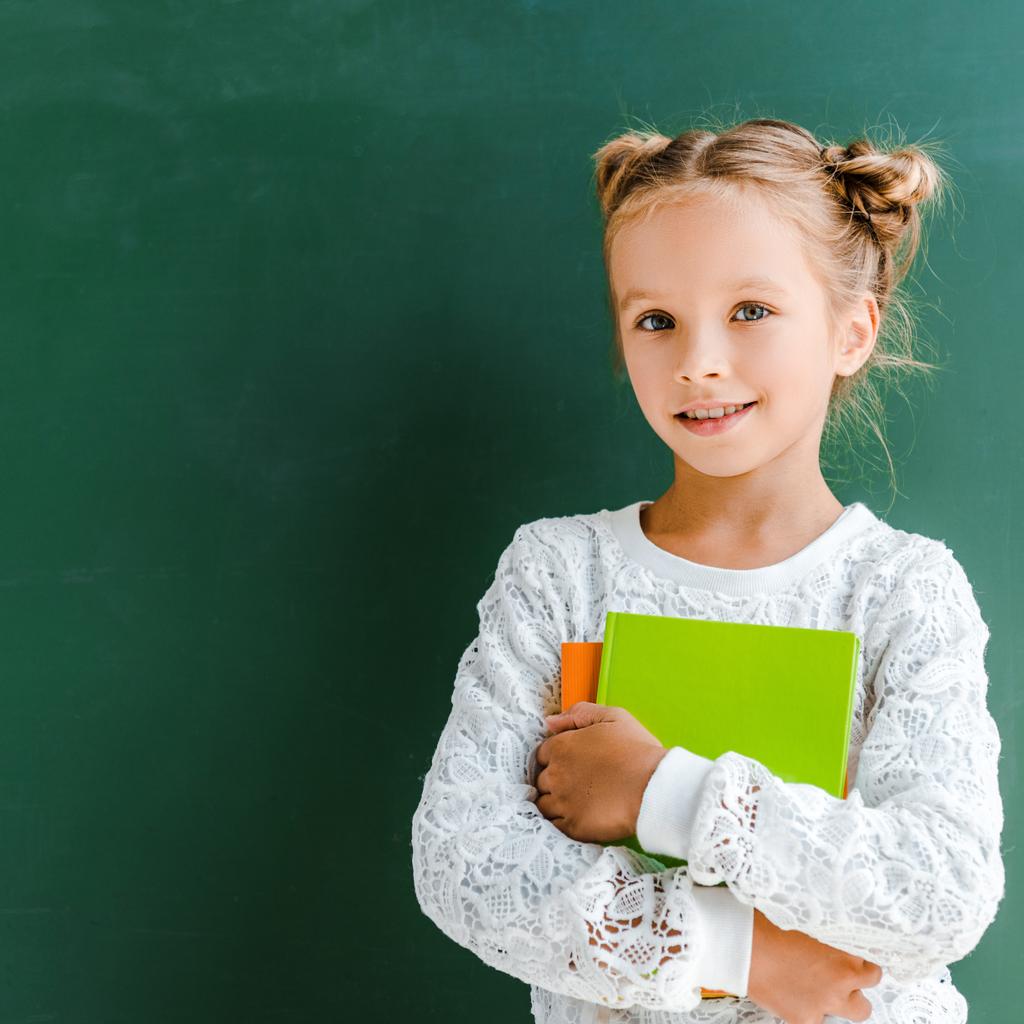 onnellinen koulutyttö hymyilee seisoessaan kirjoja vihreä
  - Valokuva, kuva