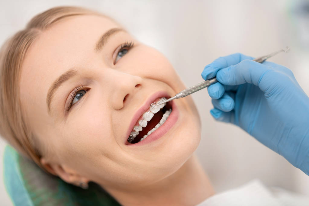Ο ασθενής διορθώνει τα ορθοδοντικά σιδεράκια της στην οδοντιατρική κλινική. - Φωτογραφία, εικόνα