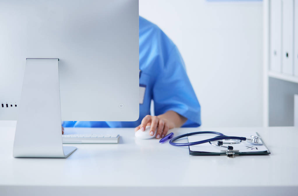 Donna medico sconosciuto riempiendo modulo medico mentre seduto alla scrivania in ufficio ospedaliero
 - Foto, immagini