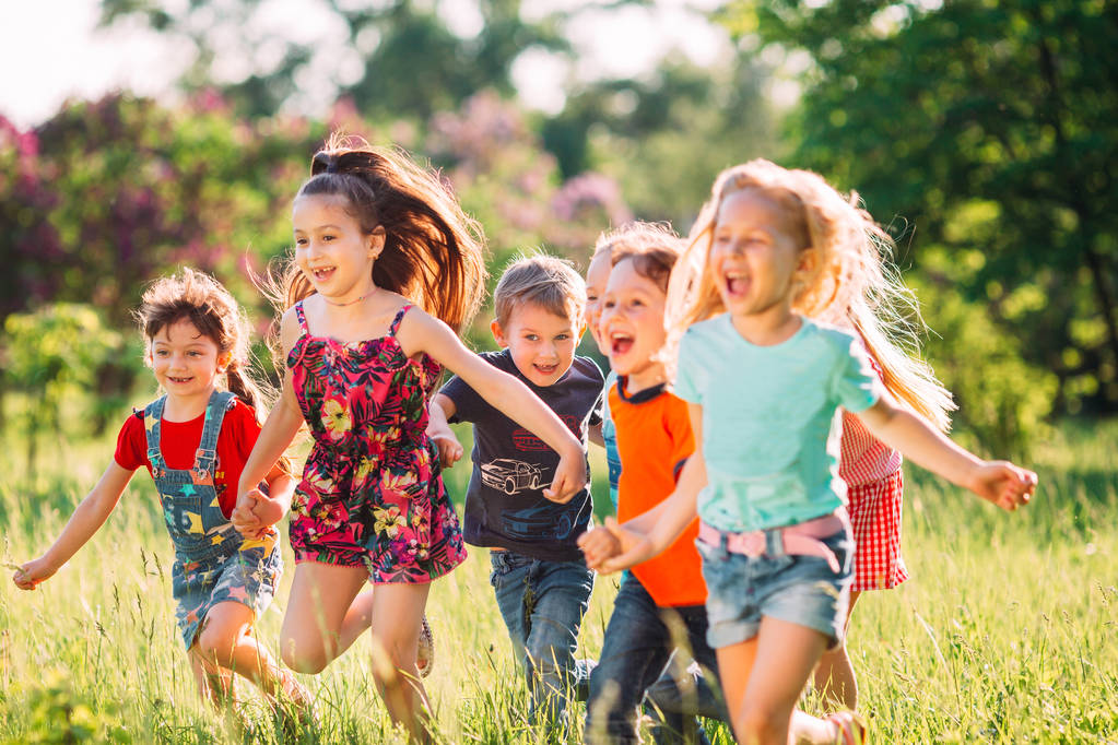 Большая группа детей, друзей мальчиков и девочек, бегающих в парке в солнечный летний день в повседневной одежде . - Фото, изображение