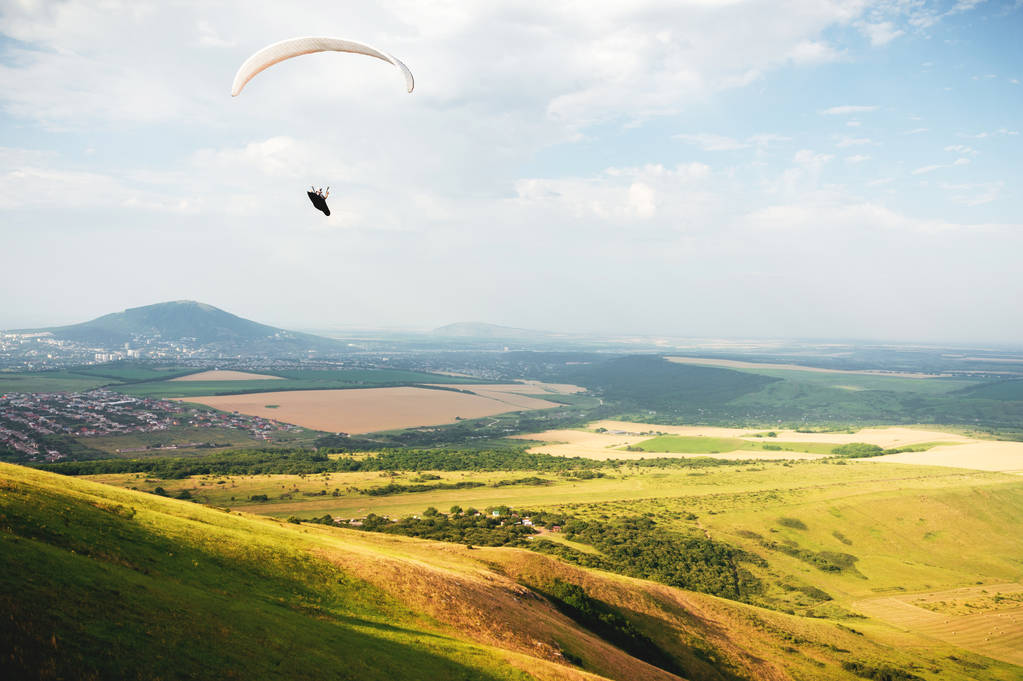 Paralotnia leci na niebie w garniturze kokonu na paralotni nad kaukaskim krajobrazom z wzgórzami i górami. Paralotniarstwo koncepcja sportu - Zdjęcie, obraz