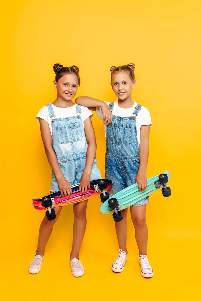Kaksi teini-ikäistä, tyylikkäät lapset, jotka poseeraavat rullalaudalla
 - Valokuva, kuva