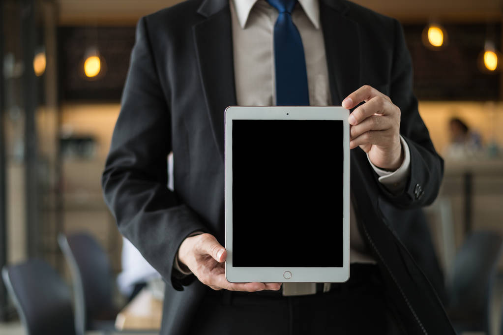 επιχειρηματίας φορούν μαύρο κοστούμι κρατώντας ένα tablet με κενή οθόνη στο γραφείο. με μαύρο χώρο αντιγραφής για κείμενο. - Φωτογραφία, εικόνα