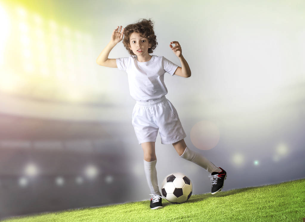 Chłopiec z piłką nożną na zielonej trawie. Podekscytowany małym chłopcem malucha grając w piłkę nożną na boisku przed jasnym tłem. Aktywna koncepcja pasji dzieciństwa i sportu. Oszczędność miejsca - Zdjęcie, obraz