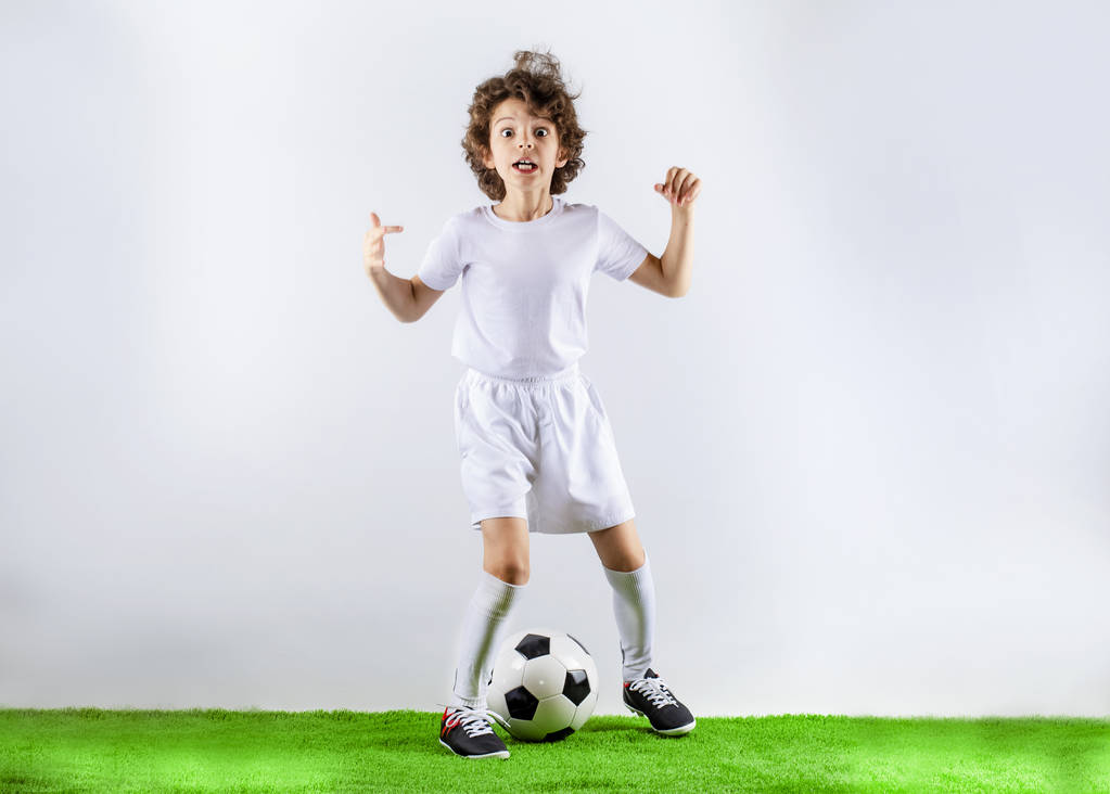 Niño con pelota de fútbol en la hierba verde. Emocionado niño pequeño jugando al fútbol en el campo de fútbol contra el fondo claro. La infancia activa y el concepto de pasión deportiva. Ahorrar espacio
 - Foto, imagen