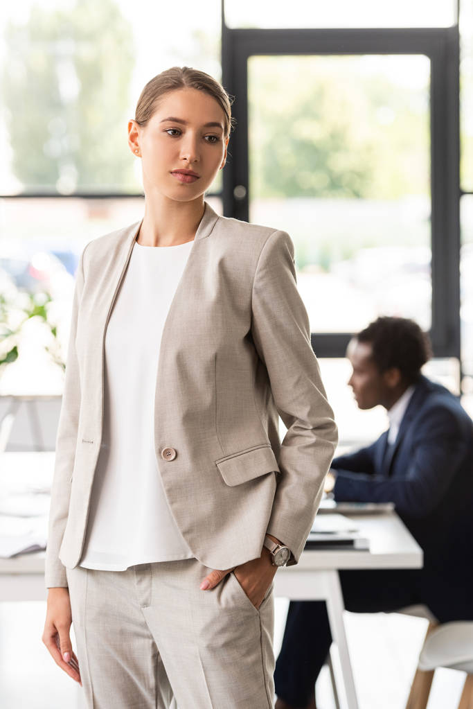 mujer de negocios pensativa en ropa formal de pie con la mano en el bolsillo en la oficina
 - Foto, imagen