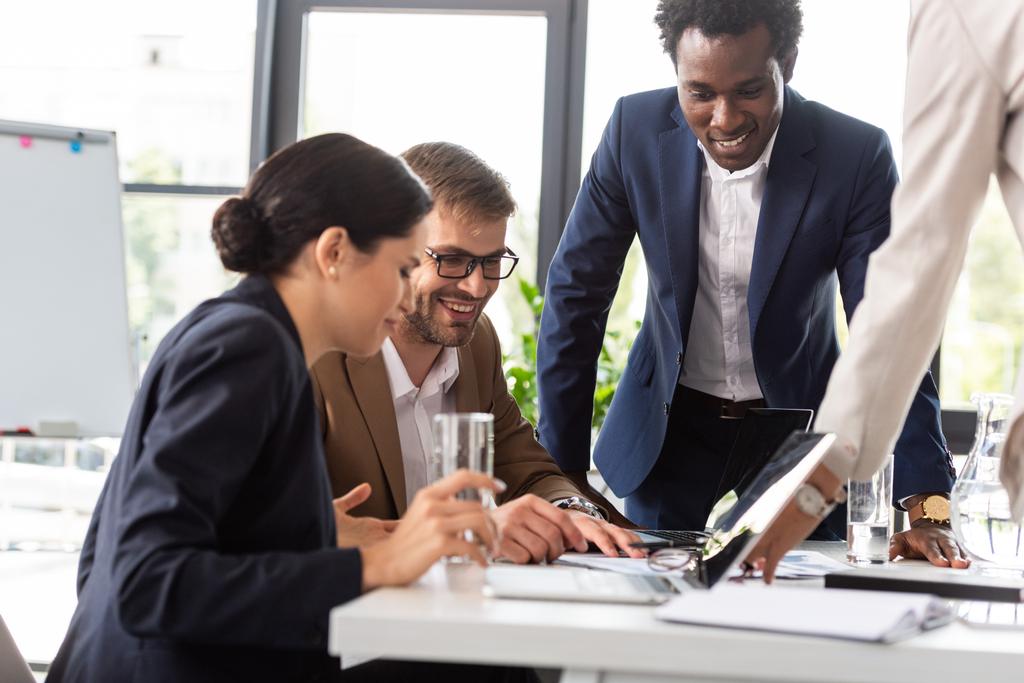 частичный взгляд улыбающихся мультиэтнических бизнесменов в формальной одежде за столом во время конференции в офисе
 - Фото, изображение