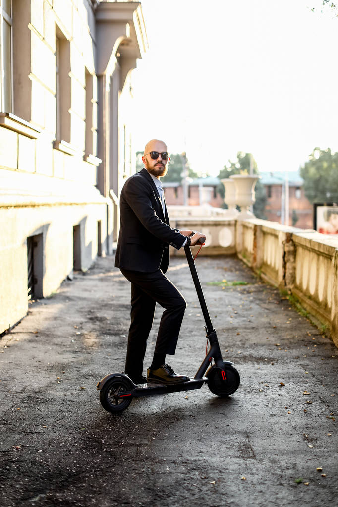 Atractivo hombre de negocios montando un patinete scooter en el fondo del paisaje urbano
 - Foto, imagen