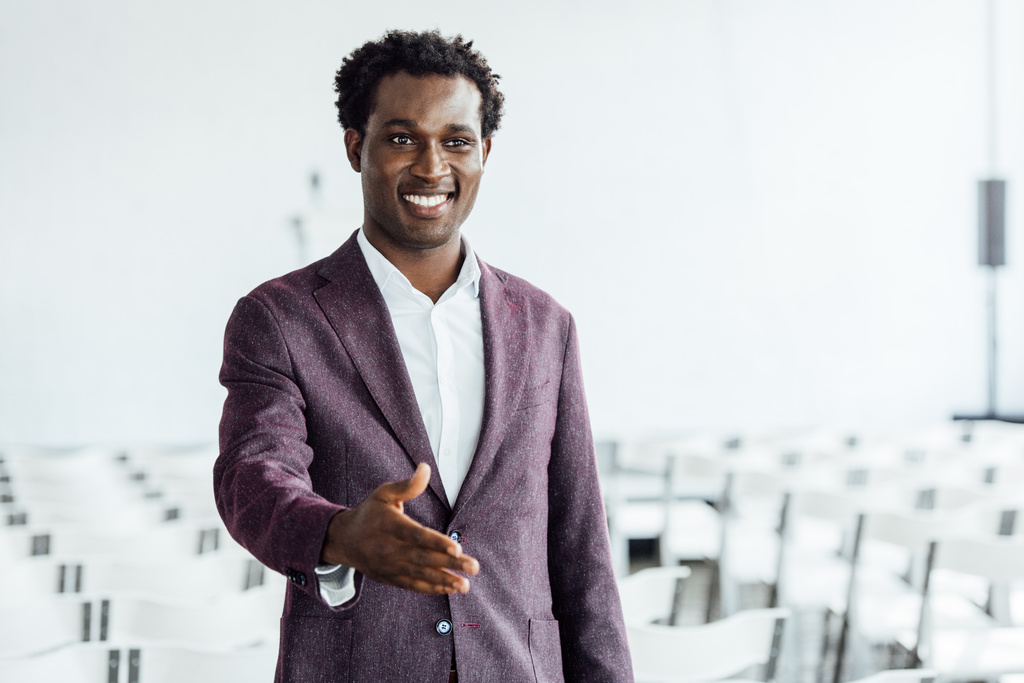 empresário afro-americano em desgaste formal com mão estendida sorrindo na sala de conferências
 - Foto, Imagem