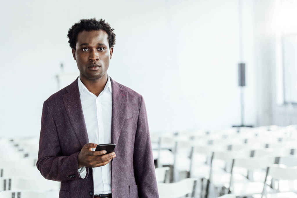 Африканский американский бизнесмен в формальной одежде держит смартфон в конференц-зале
 - Фото, изображение