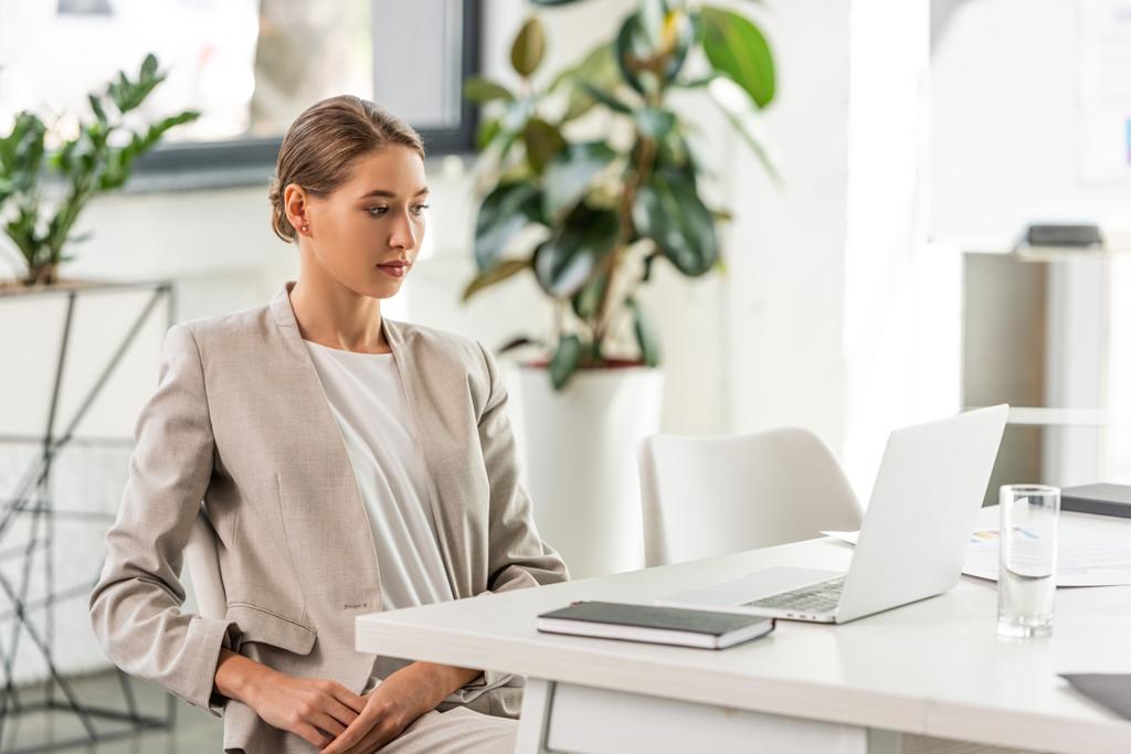 attraktive Geschäftsfrau in festlicher Kleidung sitzt und auf Laptop schaut  - Foto, Bild