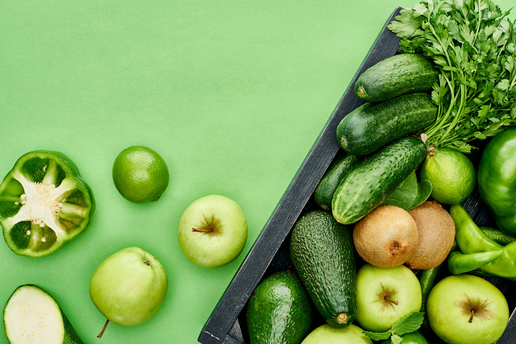 top view of apples, avocados, cucumbers, peppers, kiwi, greenery in wooden box - Photo, Image