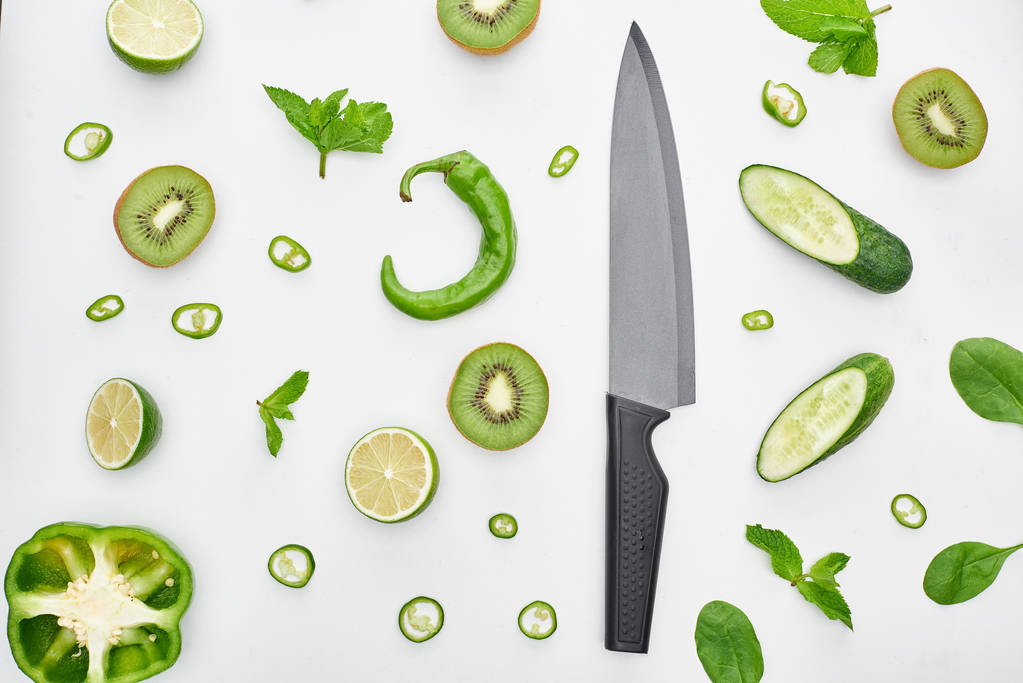  top view of knife, fresh cucumbers, kiwi, limes, peppers and greenery  - Photo, Image
