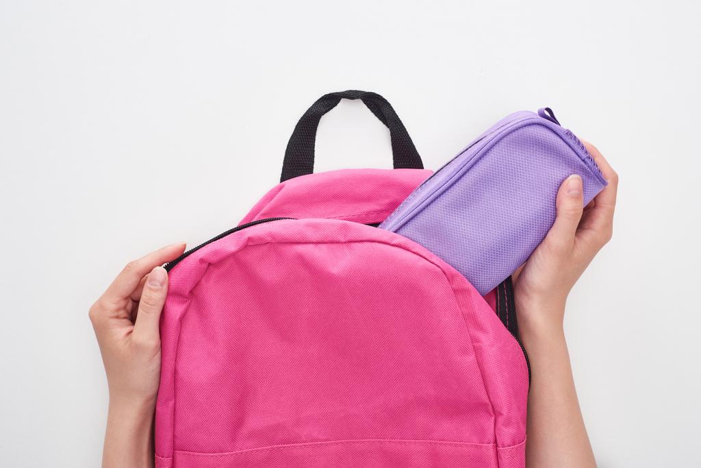 白に隔離されたピンクのスクールバッグから紫色の鉛筆ケースを取る女子高生の部分的なビュー - 写真・画像