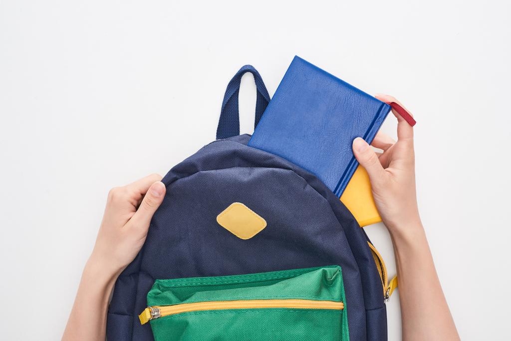 Обрезанный вид школьницы взяв блокнот из синей школьной сумки изолированы на белом
 - Фото, изображение