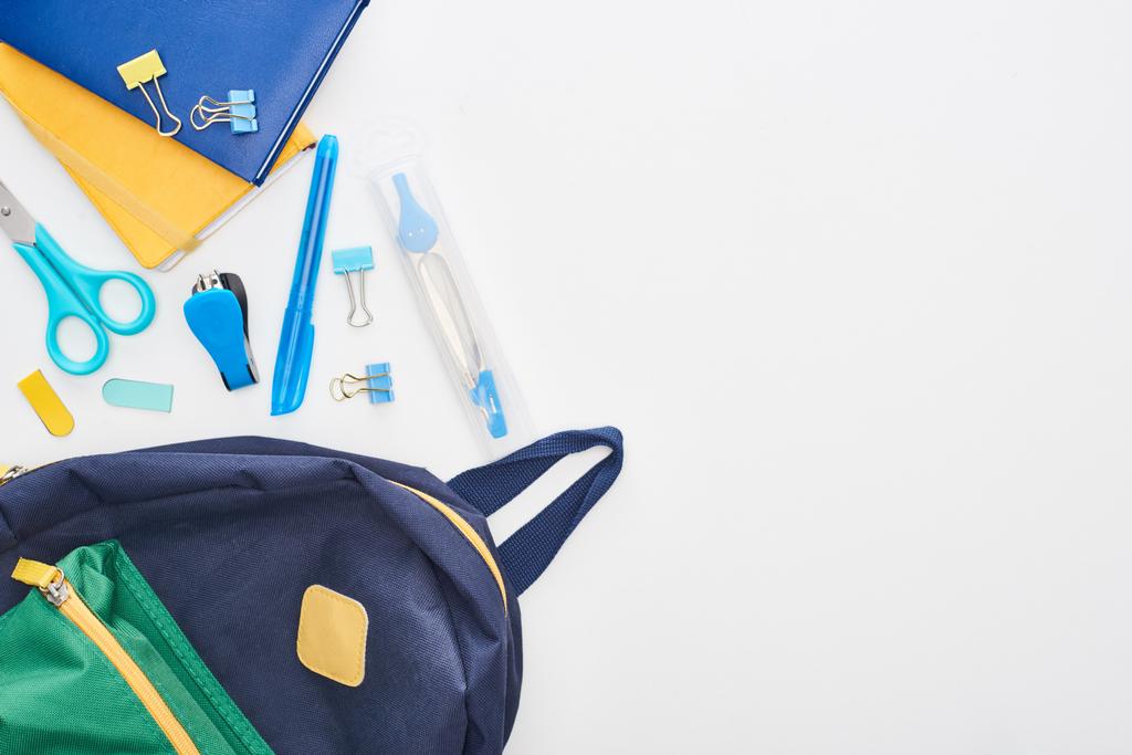 Μπλε σχολική τσάντα κοντά στις αγγελίες, ψαλίδι και διαφορετικές σχολικές προμήθειες απομονώνονται σε λευκό  - Φωτογραφία, εικόνα
