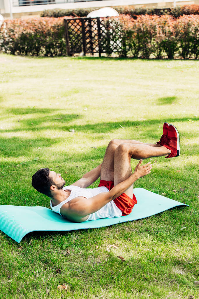 pohledný muž v sportovní přísaze dělá ABS na fitness rohoži venku  - Fotografie, Obrázek