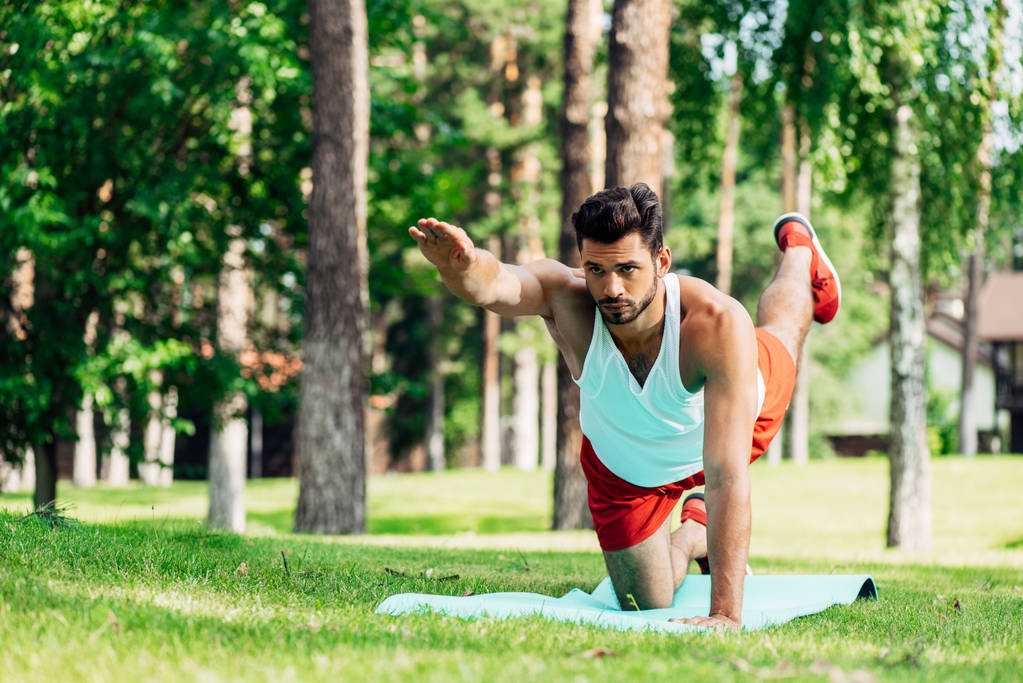 serious sportsman working out on fitness mat in park  - Photo, Image