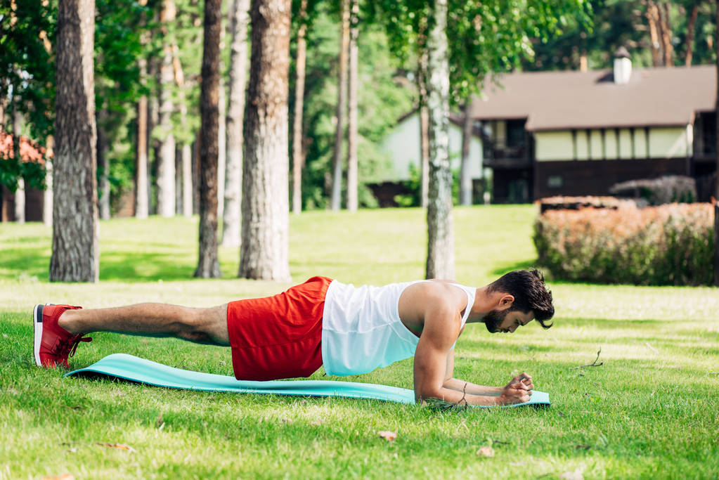 προφίλ του όμορφος άνθρωπος κάνοντας σανίδα άσκηση στο χαλάκι γυμναστικής  - Φωτογραφία, εικόνα