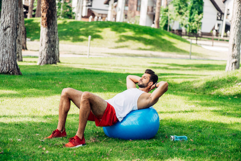 spor şişesi yakınında fitness topu üzerinde çalışan sakallı adam  - Fotoğraf, Görsel