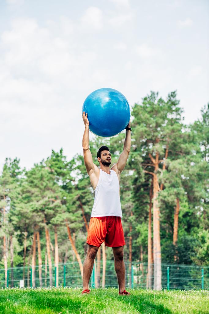 apuesto deportista haciendo ejercicio mientras sostiene la pelota de fitness en el parque
  - Foto, Imagen