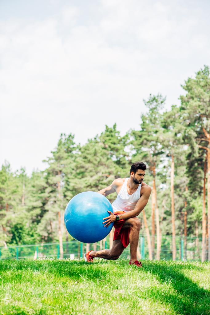 handsome sportsman exercising with fitness ball in park  - Photo, Image