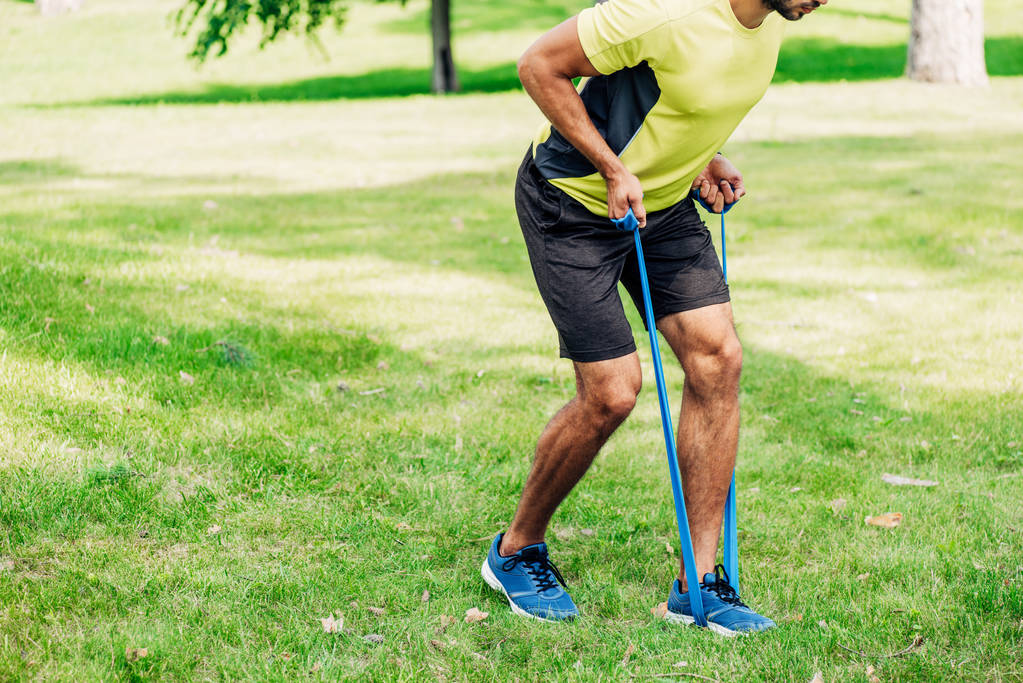 Ausgeschnittene Ansicht eines bärtigen Mannes, der mit Aufhängebändern im Park trainiert  - Foto, Bild