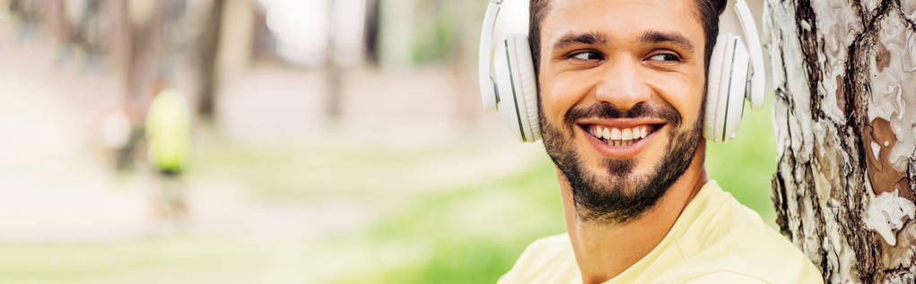 Panoramaaufnahme eines fröhlichen bärtigen Mannes, der Musik über Kopfhörer hört  - Foto, Bild