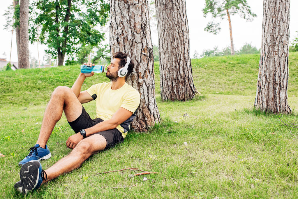 homem bonito com olhos fechados bebendo água perto de árvores
  - Foto, Imagem