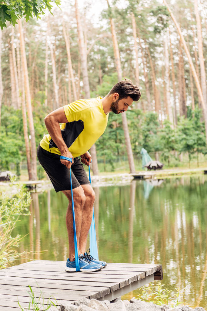 hombre barbudo guapo haciendo ejercicio con correas de suspensión cerca del lago en el bosque
  - Foto, imagen