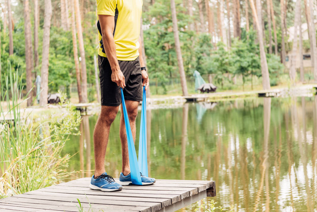 Ausgeschnittene Ansicht eines Mannes, der in der Nähe des Sees mit Spanngurten trainiert  - Foto, Bild