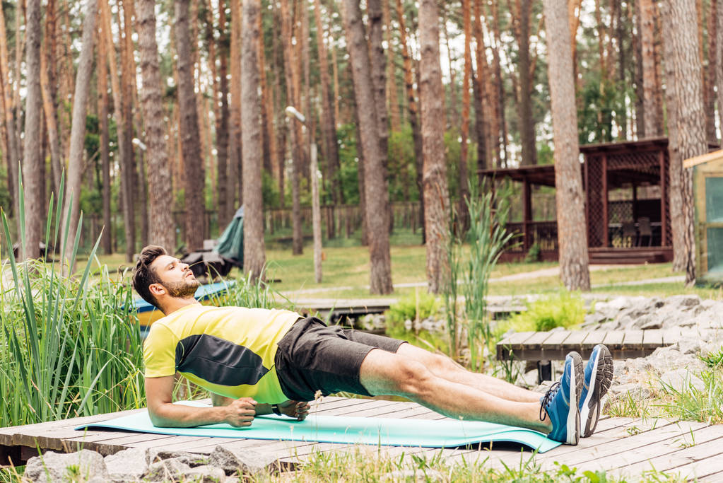 Sportman trainen op fitness mat in bos in de buurt van bomen  - Foto, afbeelding